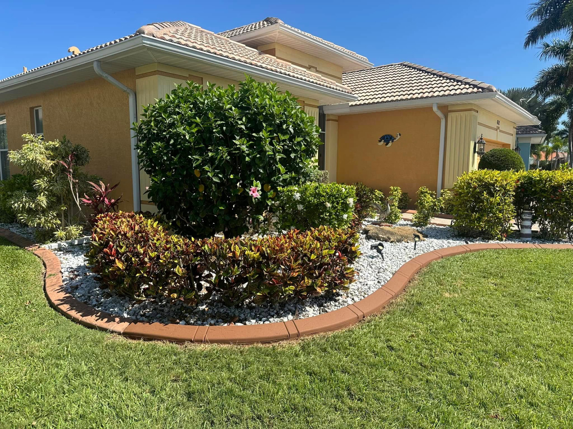 Southwest Florida home with decorative concrete curbing, white rock, and colorful landscaping island